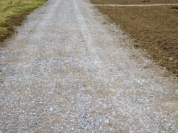 A gravel driveway bordered by grass and soil.